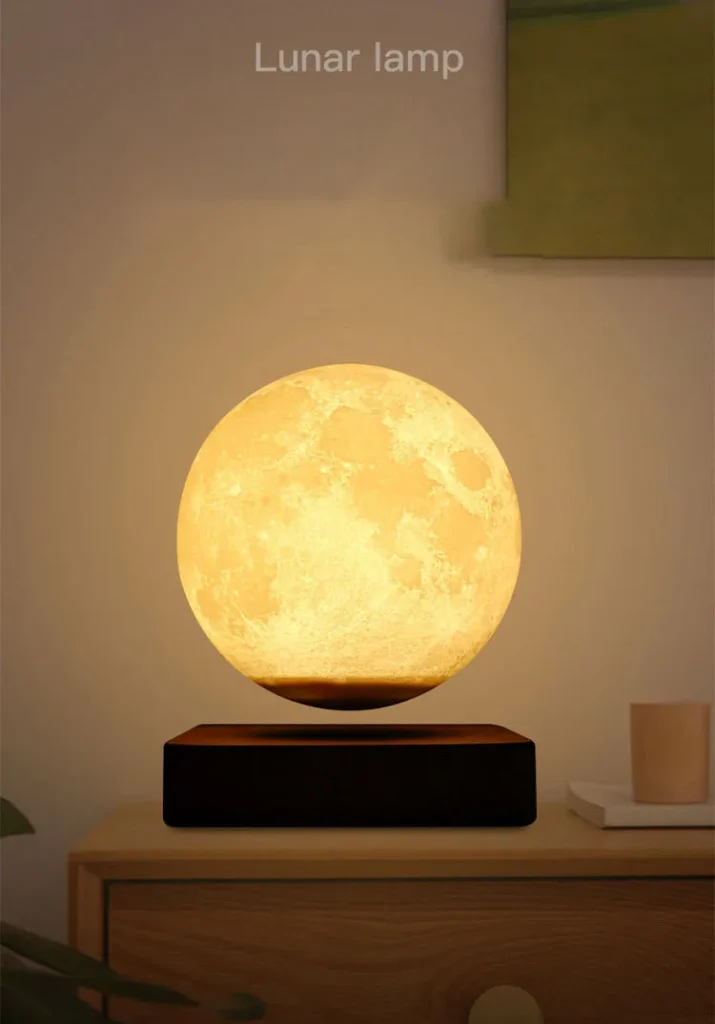 A lunar lamp emitting a warm, yellow light, placed on a wooden surface. The lamp is spherical, resembling the moon, and it appears to be levitating above a dark base. Text above reads "Lunar lamp."