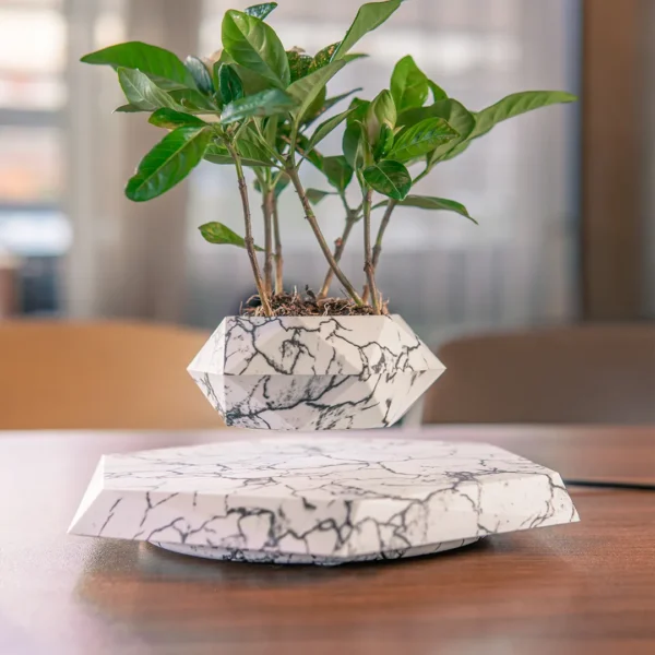 Hot Selling Air Bonsai Magnetic Levitating Flower Pot Floating Plant Pot Creative Gifts For Home Decoration 7 A small plant in a geometric pot levitates above a matching marble-patterned base, sitting on a wooden table.