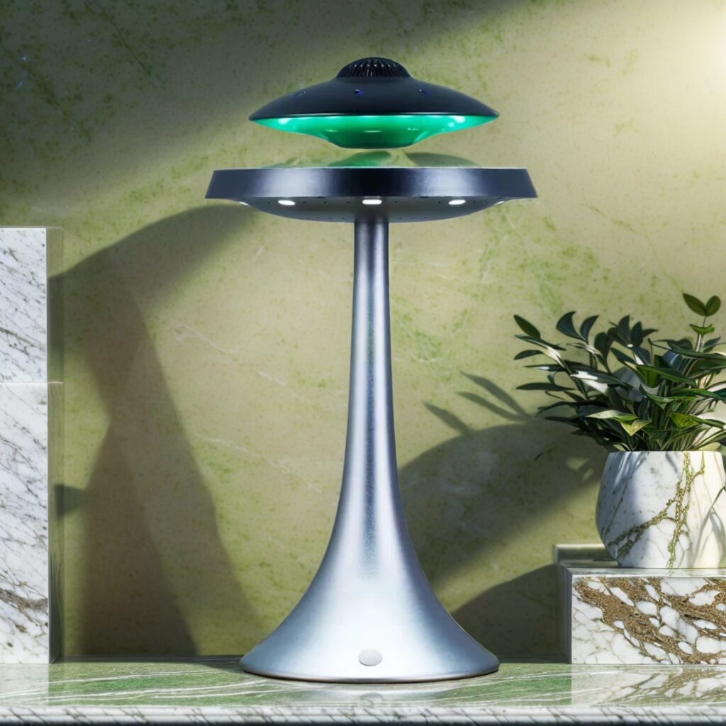 A Floating UFO Speaker, designed with a green and black UFO-shaped light fixture that appears to be levitating above its cone-shaped base, is placed on a marble surface with a potted plant beside it.