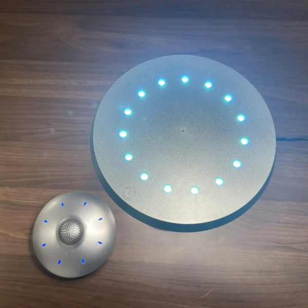 UFO Speaker Super Cool Levitating Speaker Magnetic Floating UFO Speaker Music Player with RGB Color Table Lamp 6 Two circular electronic devices on a wooden surface; one device has an illuminated ring with blue lights, while the other has small blue light dots and a central metallic pattern.