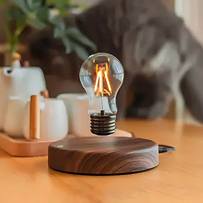 Levitating light bulb above a wooden base on a table, with a tea set and blurred background elements.