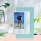 A floating photo frame displaying a couple in casual summer attire at the beach, surrounded by potted green plants and set on a table.