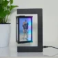 A levitating photo frame with a couple's picture, featuring a modern black design. A potted plant sits beside it on a white surface.