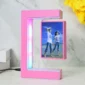 A pink C-shaped LED photo frame with a couple's picture inside. The frame is on a white surface, next to a stack of books and a yellow flower.