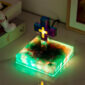 The Floating Cross Nightlight, shaped like a Greek cross and adorned with multiple colors, rests on a glowing square base with a cosmic design.