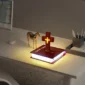 A desk with a decorative cross lamp on top of an illuminated book, next to a small giraffe figurine and a pen holder.