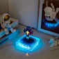 A glowing decorative cross on a blue illuminated base, surrounded by astronaut figurines and books on a table.