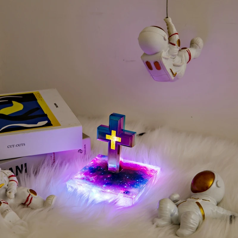 Three astronaut figurines around a light-up cross on a fluffy surface, with a book nearby.