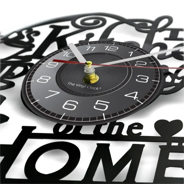 The Kitchen The Heart of The Home Inspired Vinyl Record Clock Modern Design Vinyl Wall Watch Kitchen Decor Noiseless Timepieces 2 Close-up of a round vinyl-themed wall clock with white numbers and hands on a black face. The background features black decorative text and shapes.