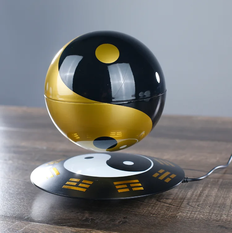 A Levitating Magic Ball featuring a yin-yang theme with a black and gold design, floating above a complementary base on a wooden surface.