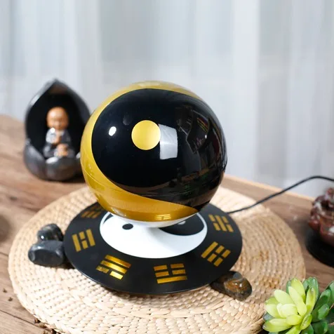 A Levitating Magic Ball in black and gold hovers above a device on a woven mat, surrounded by decorative stones and a small statue.