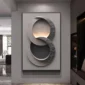 A modern, abstract wall art piece with interlocking circular shapes in gray tones, illuminated by soft lighting, hanging in an elegant interior.