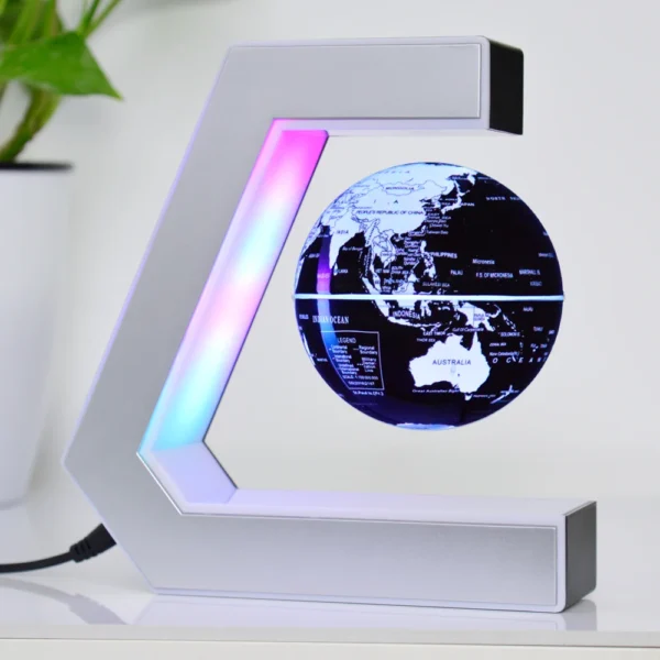 Plastic World Geography Map Rotating Globe Magnetic Levitating Floating Globe for Kids Education Home Office Desktop Decoration - EK3-white lighting black white globe 13 A small black and white globe floats and rotates within a C-shaped magnetic levitation stand, with multicolored LED lights illuminating the setup. A potted plant sits in the background.
