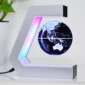 A small black and white globe floats and rotates within a C-shaped magnetic levitation stand, with multicolored LED lights illuminating the setup. A potted plant sits in the background.