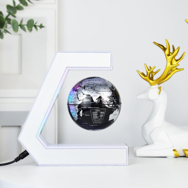 Plastic World Geography Map Rotating Globe Magnetic Levitating Floating Globe for Kids Education Home Office Desktop Decoration 3 A black and silver globe levitates within a C-shaped magnetic holder on a white desk, next to a white decorative deer with gold antlers.